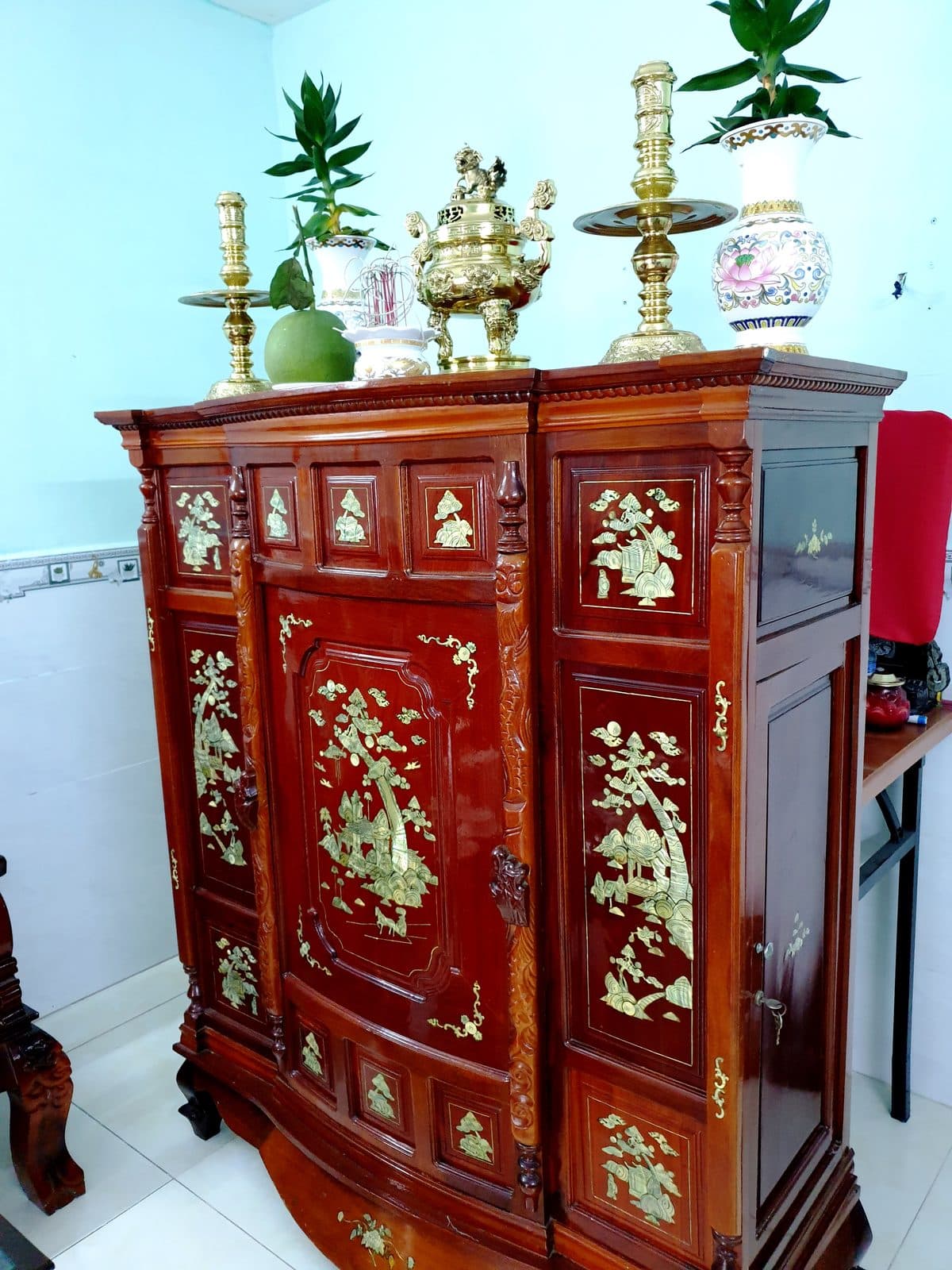 Tủ thờ gỗ khảm xà cừ, trên nóc có lư hương đồng, hai chân nến đồng, hai bình cây xanh, quả bưởi và bát hương.