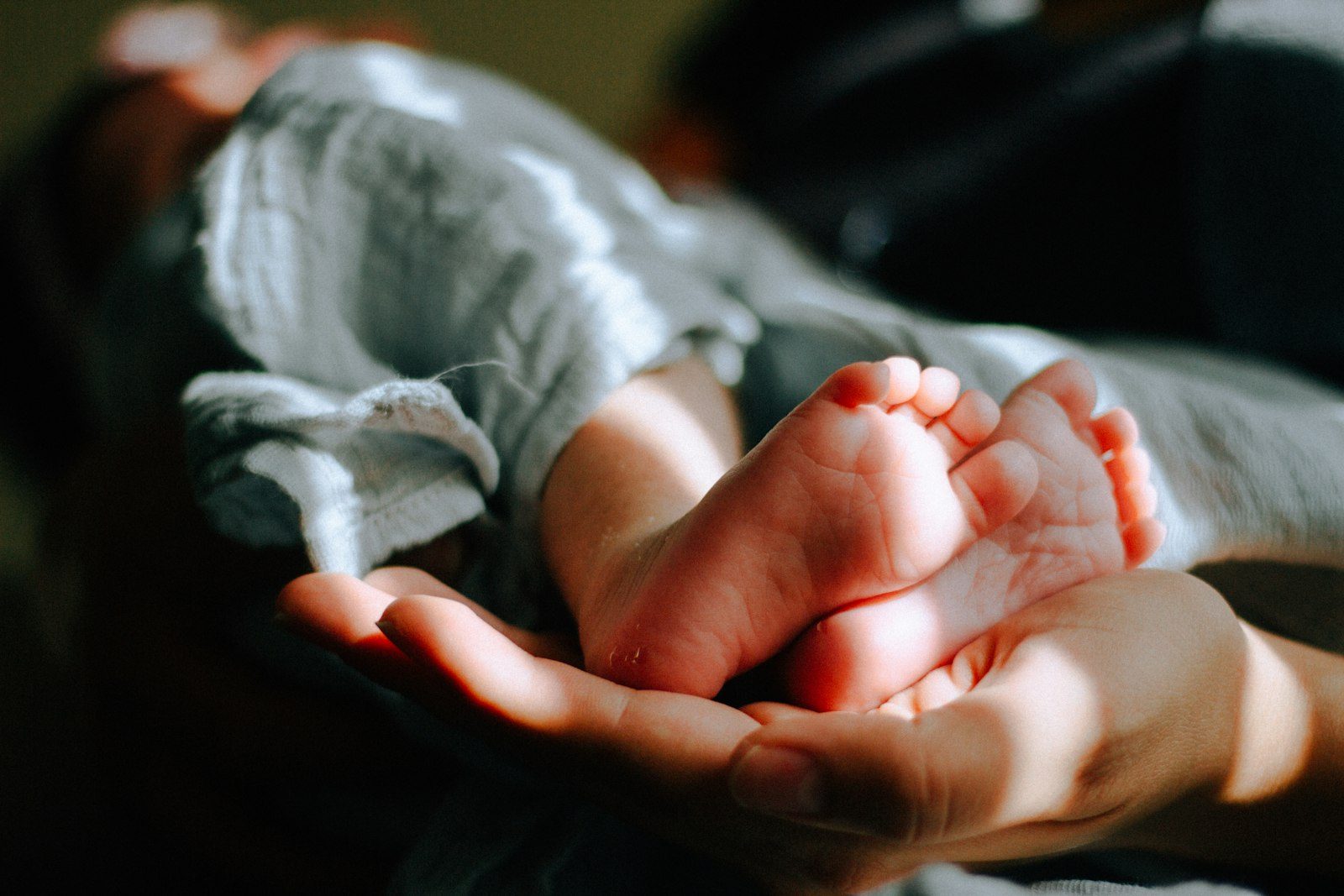 Đôi tay nâng niu bàn chân trẻ sơ sinh dưới nắng ấm